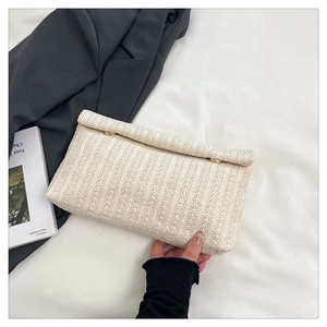 Detail of cream woven envelope clutch featuring gold magnetic buttons and straw texture