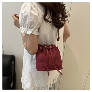 Dettaglio borsa a secchiello in lana bordeaux con chiusura a coulisse e finiture dorate
