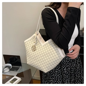 Detail of white tote bag with grey monogram print and golden metal charm for commute