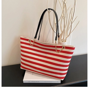 Detail of red and white striped canvas tote bag with black straps and gold chain accents