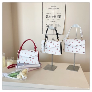 Trois sacs blancs à motif cerise avec poignées nouées dans un décor intérieur élégant