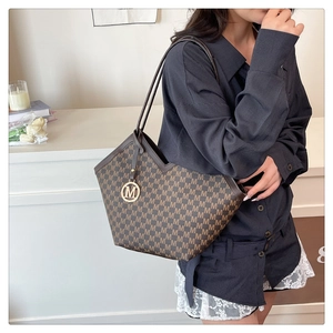 Detail of a brown monogram tote bag with gold M pendant and slim shoulder strap