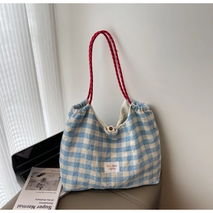 Close-up of blue plaid canvas tote bag with red braided handles and brand label detail