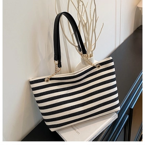 Detail of striped canvas tote bag showing black leather strap with gold chain link