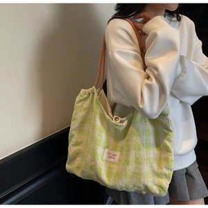 Dettaglio della borsa tote a scacchi verdi con toppa colorata e tracolla intrecciata
