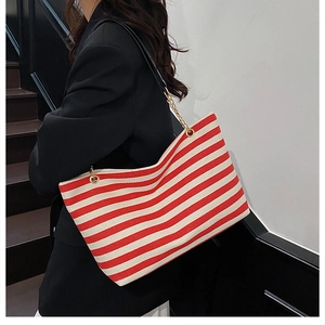 Detail of red and white striped canvas tote bag with gold chain strap on model shoulder