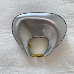 Vue à plat d'un sac demi-lune argenté avec fermetures dorées sur tissu plissé blanc