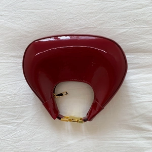 Détail du sac croissant bordeaux brillant avec fermeture éclair dorée et verrou chic