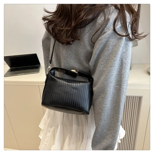 Detail of a chic black pleated handbag featuring a top handle and adjustable strap