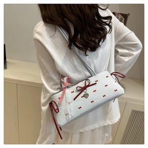 Détail d'un sac à bandoulière blanc avec nœuds rouges, pendentif cœur et ruban dentelle