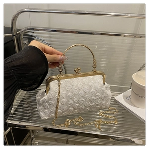 Detail der weißen Spitzen-Abendtasche mit goldenem Metallgriff und Rosen-Textur
