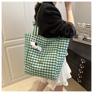 Detail of green gingham canvas tote bag featuring a metal nameplate and plush dog charm