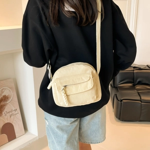 Minimalist beige corduroy crossbody bag with wide strap and braided zipper detail