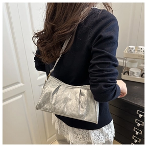 Detail of silver metallic pleated cloud bag with glossy texture on model's shoulder