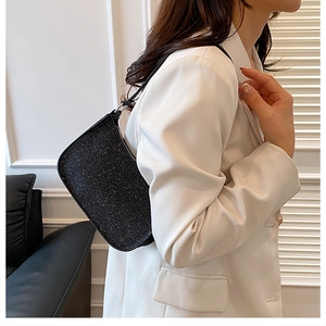 Détail du sac à bandoulière noir scintillant porté sur un blazer blanc élégant