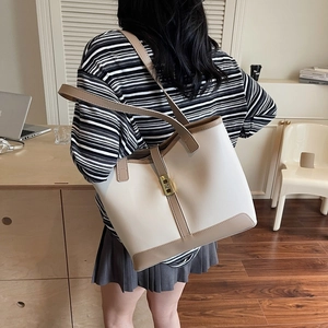 Minimalist beige tote bag with brown handles and gold clasp shown on person in office