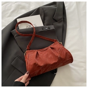 Detail of reddish-brown pleated baguette bag with glossy texture and gold metal buckle
