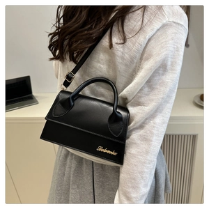 Detail of a black minimalist leather crossbody bag with a gold metal logo and sleek flap