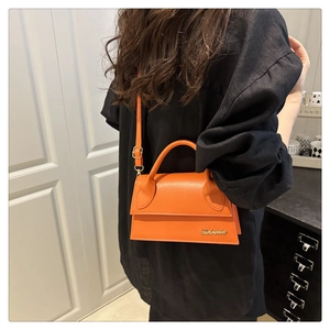 Detail van de oranje crossbodytas met metalen logo en elegant handvat bovenaan