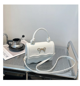 Close-up of white leather handbag with gold bow detail and stylish wavy edge flap