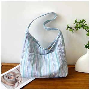 Détail du sac à bandoulière en nylon rayé avec poches avant pratiques sur une table en bois