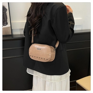 Detail of a beige crossbody bag featuring vintage metal rivets and rectangle logo plaque