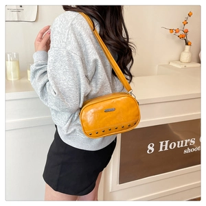 Detail view of ginger yellow crossbody camera bag featuring silver rivets and metal plaque