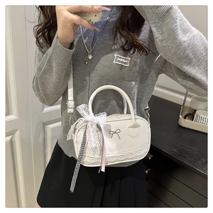 Detailed view of white shell bag featuring lace trim and a metallic bow accessory