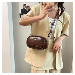 Retro brown leather crossbody bag with metal rivets shown on a beige outfit