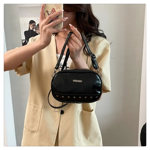 Detail of black glossy leather crossbody bag with silver metal studs and logo plaque