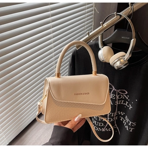 Detail of beige textured patchwork handbag with gold metal handle and logo flap
