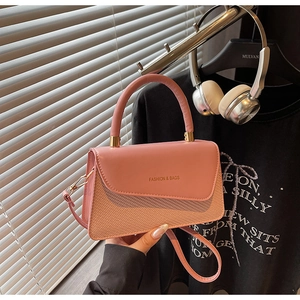 Detail showing pink crossbody bag with woven texture and top handle in casual setting
