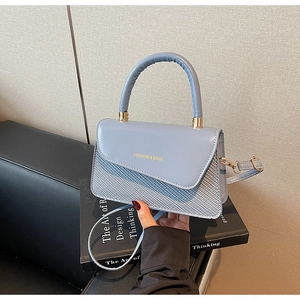 Detail of light blue square crossbody bag with woven texture and gold fashion lettering