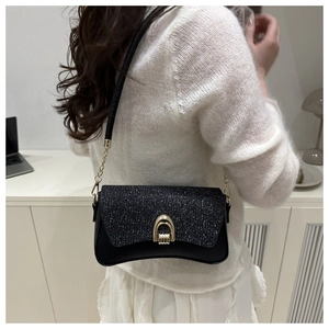 Detail of a black sequin shoulder bag featuring a gold horseshoe buckle and chain strap