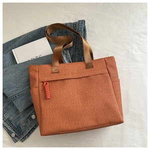 Detail of woven texture on caramel tote bag with zipper pocket and red tassel accent