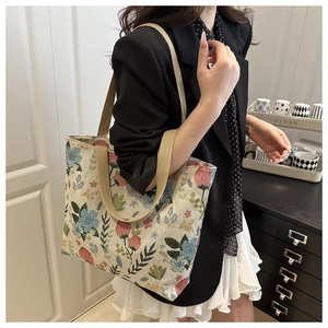 Detail view of floral embroidered canvas tote bag with woven handles on a female model