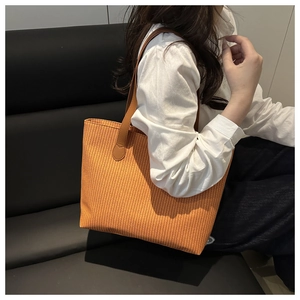 Close-up of woven orange tote bag with brown leather handles worn by a model
