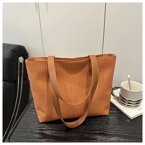 Detailed close-up of woven orange-brown tote bag texture and brown leather shoulder straps