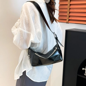 Bolso de hombro de charol negro brillante con correa ajustable llevado por una modelo