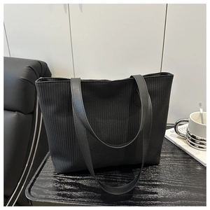 Detail of the black woven tote bag with mesh texture and long handles on a leather chair