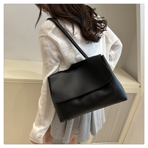 Close-up of minimalist black matte leather shoulder bag worn by model in a chic setting