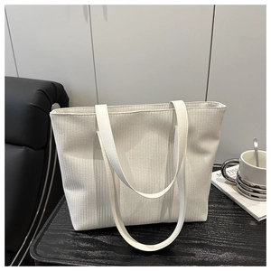 Close-up of white woven tote bag texture and faux leather straps on dark table