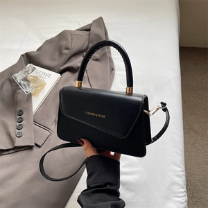 Close-up of black handbag with golden logo lettering and mixed material texture