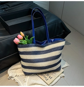 Detail of blue and white striped woven tote bag with premium leather handles on a sofa