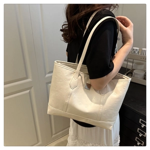 Detail of off-white PU leather tote bag with embossed patterns worn on woman's shoulder