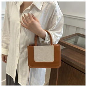 Braune Leder- und Canvas-Umhängetasche am Modell in einem minimalistischen modernen Ambiente