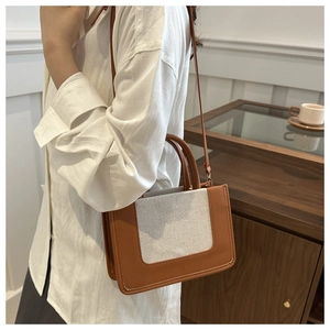 Detail of canvas and brown leather crossbody bag shown on a model in a cozy cafe setting