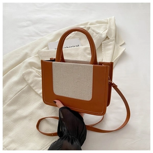 Detail einer Tasche aus braunem Leder und beigem Canvas mit verstellbarem Schultergurt