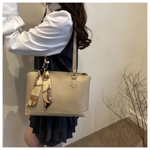 Detail of a beige tote bag with a patterned silk scarf on the handle for elegant styling