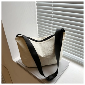 Detail of off-white nylon crescent bag with black strap resting on books by a window